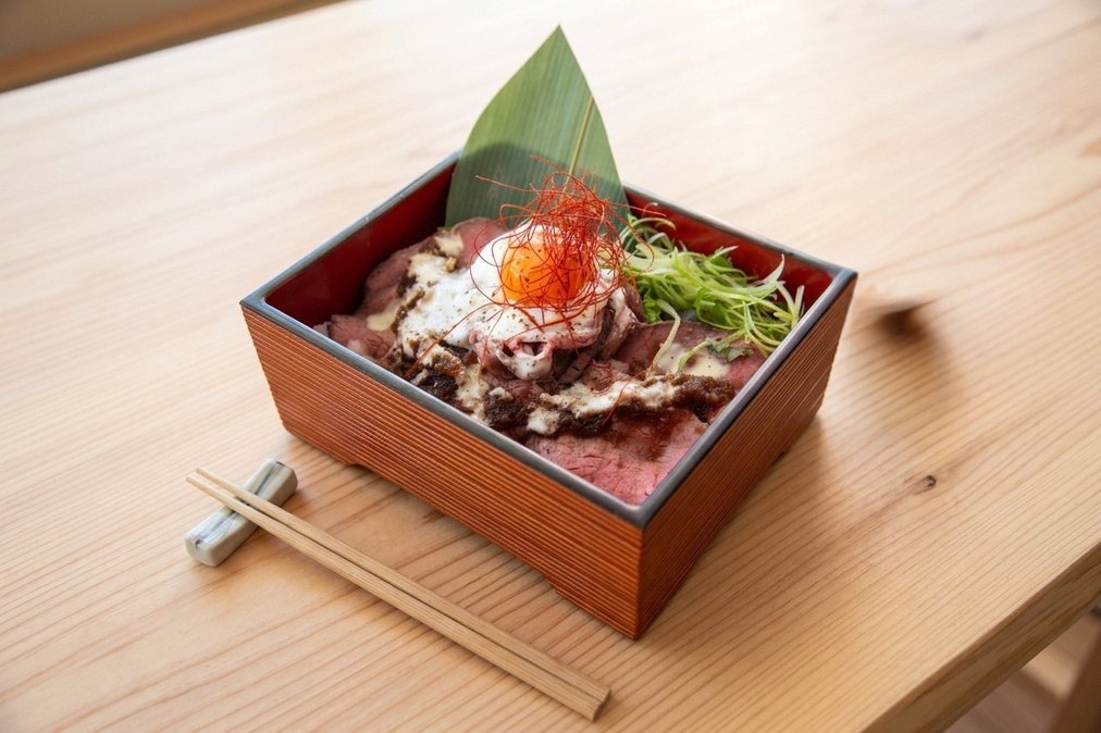 A Bentendo roast beef jyu on a wooden table with chopsticks resting alongside.